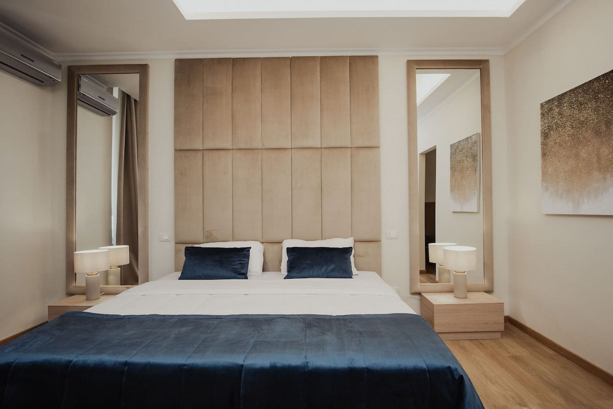A modern hotel room with a large bed, two bedside tables with lamps, a headboard with vertical panels, and a skylight above.