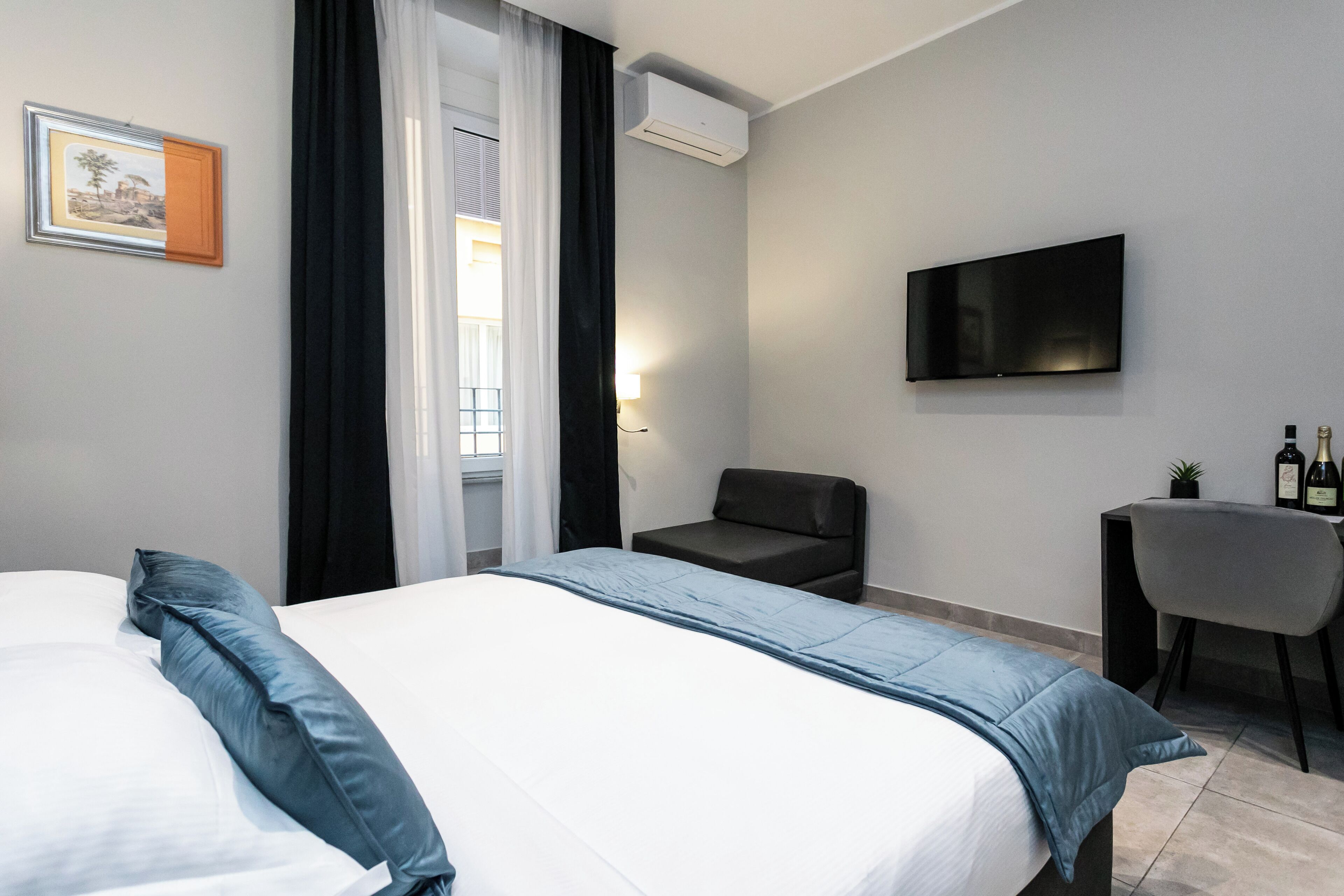 Habitación de hotel con cama, escritorio, silla, televisor y ventana con cortinas.