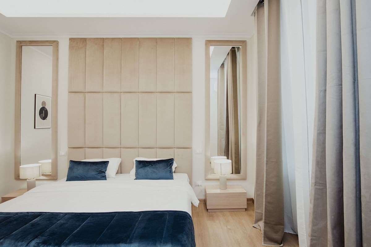A modern hotel room with a large bed, bedside lamps, a headboard, and a mirror.