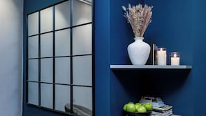 A room with a large window, a white vase with dried flowers, a shelf with books and candles, and a bowl of green apples. - Cesare ai Cavalieri Suites (Rome)