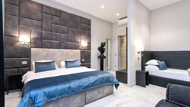 A modern bedroom with a large bed, a smaller bed, and a seating area. - Cesare ai Cavalieri Suites (Rome)
