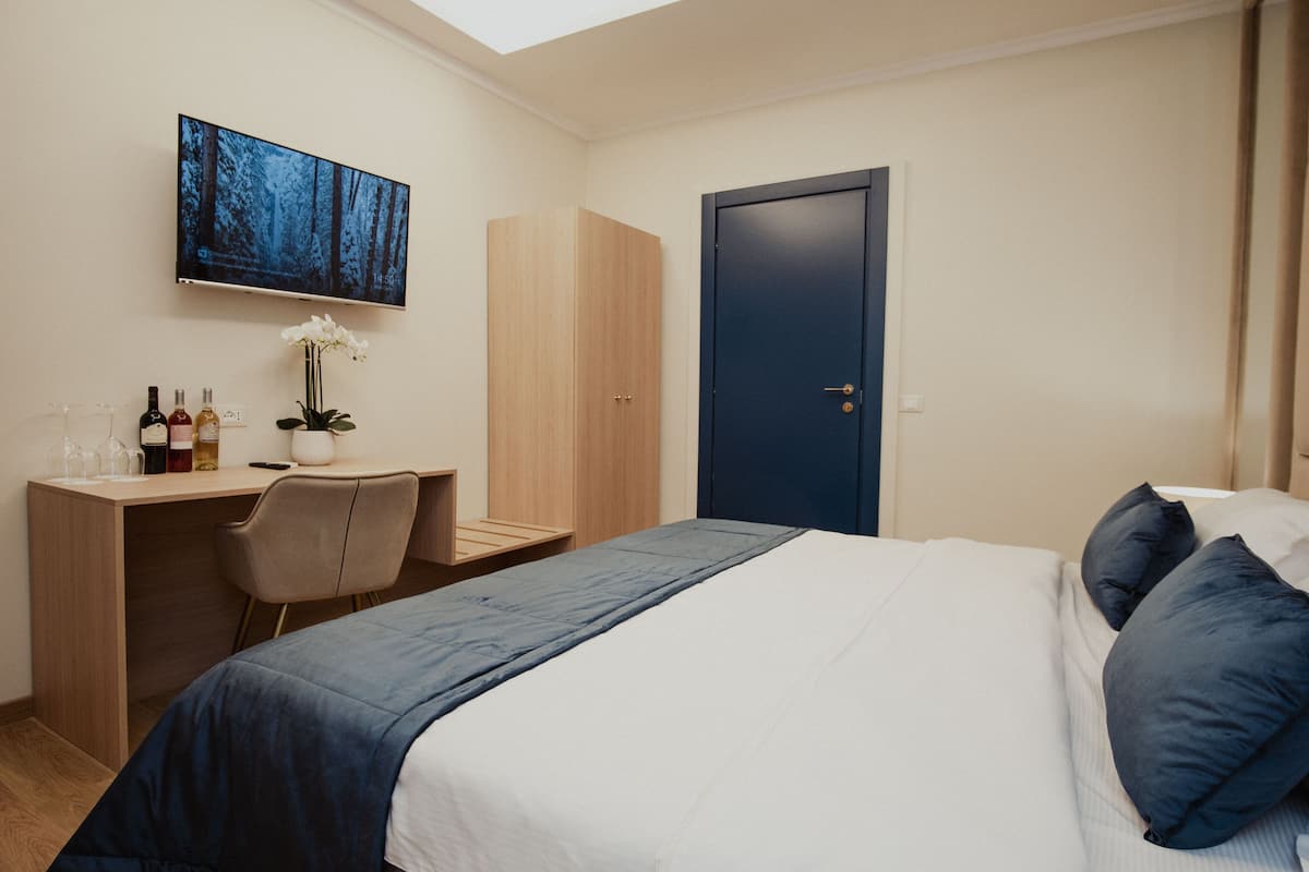 A hotel room with a bed, a desk, a chair, a TV mounted on the wall, and a door.