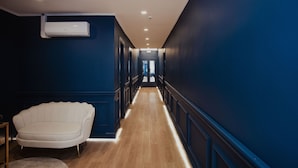 A hallway with a white upholstered chair, wooden flooring, and blue walls. - Cesare ai Cavalieri Suites (Rome)