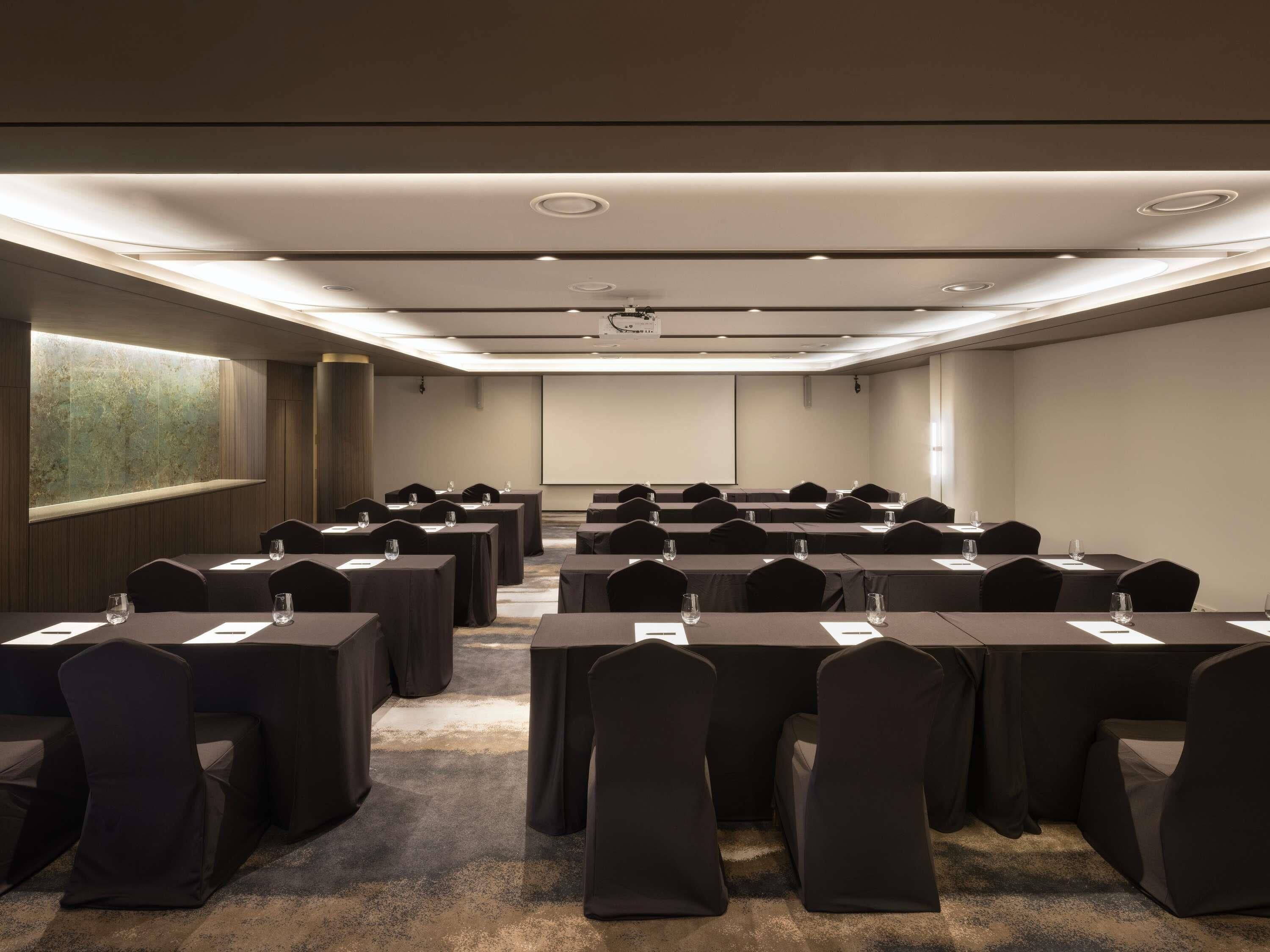 A conference room with rows of tables, chairs, and a projector screen.