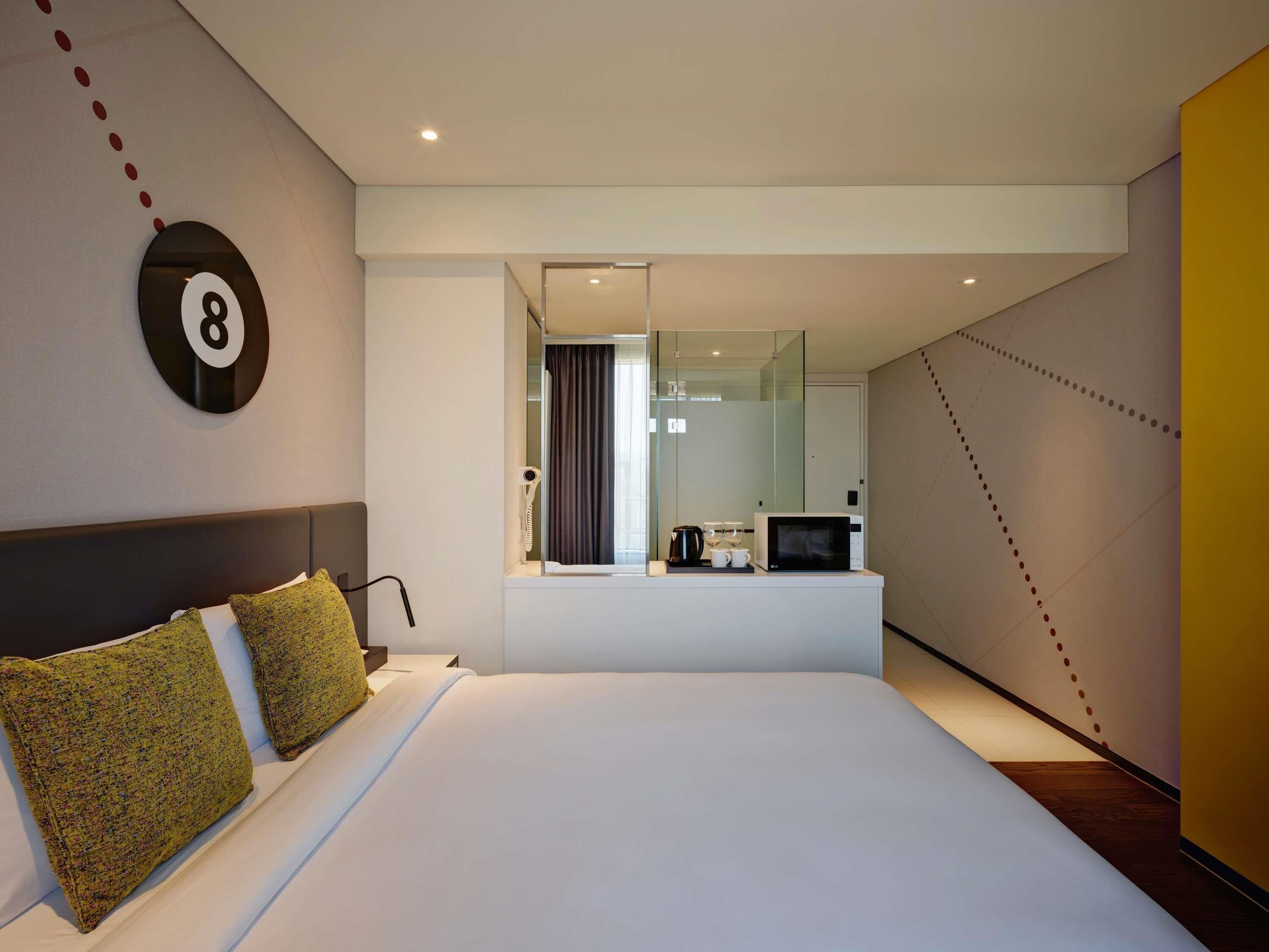 A modern hotel room with a large bed, a bedside table with a microwave, a hairdryer, and a coffee maker.