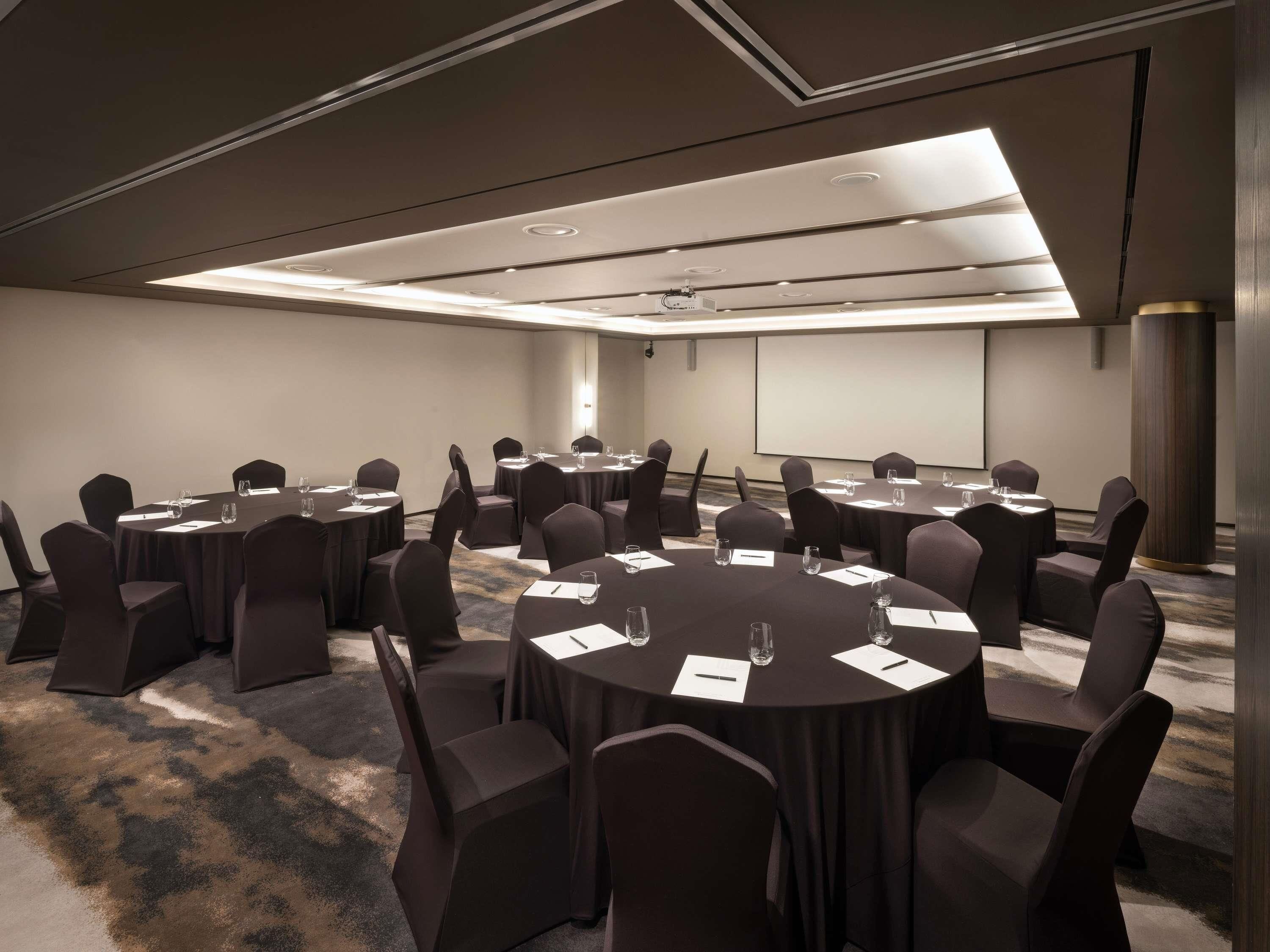 A conference room with round tables and chairs, a projector screen, and a carpeted floor.