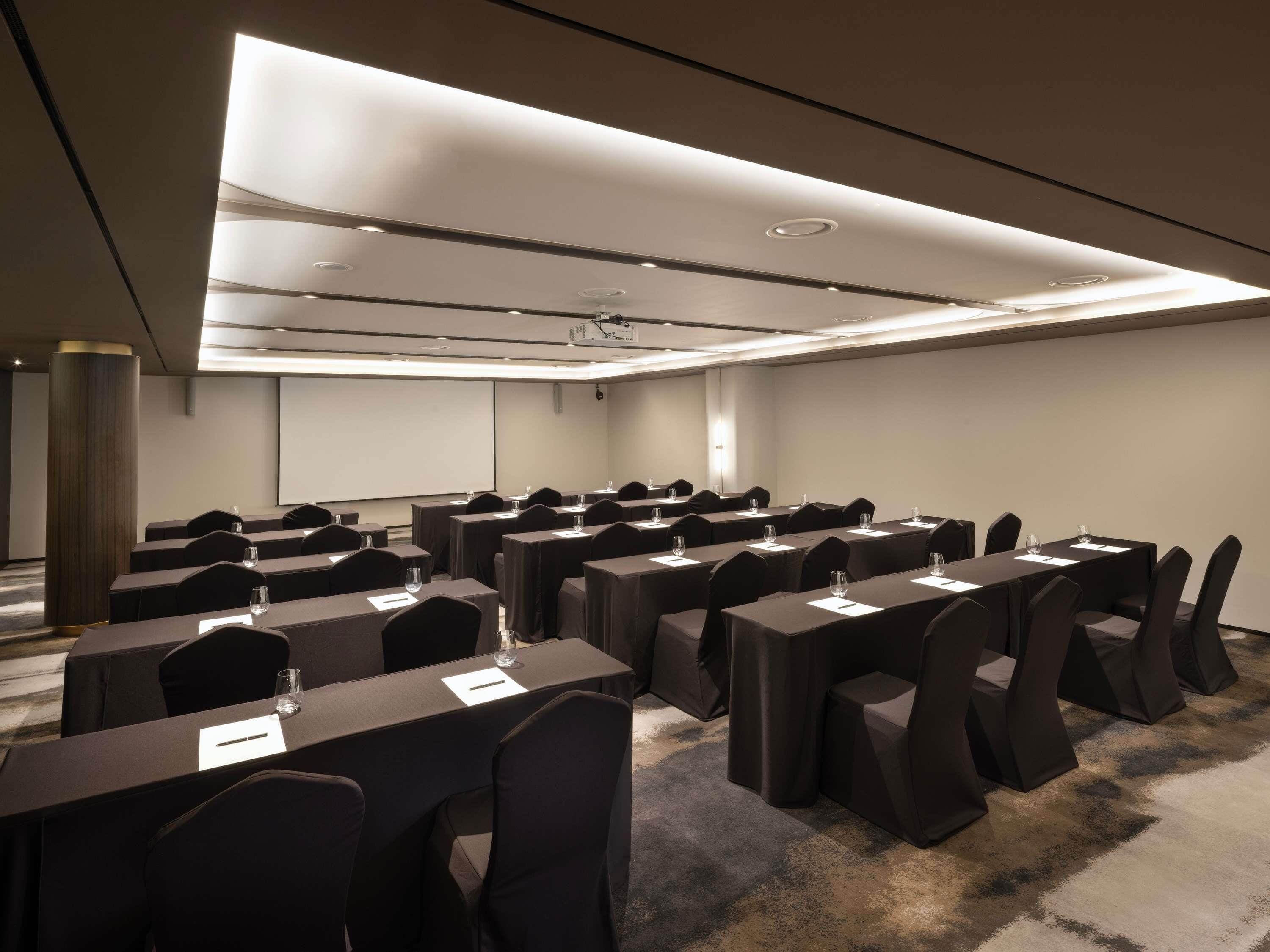 Un salón de conferencias con filas de mesas y sillas, equipado con tarjetas de nombre y vasos de agua.