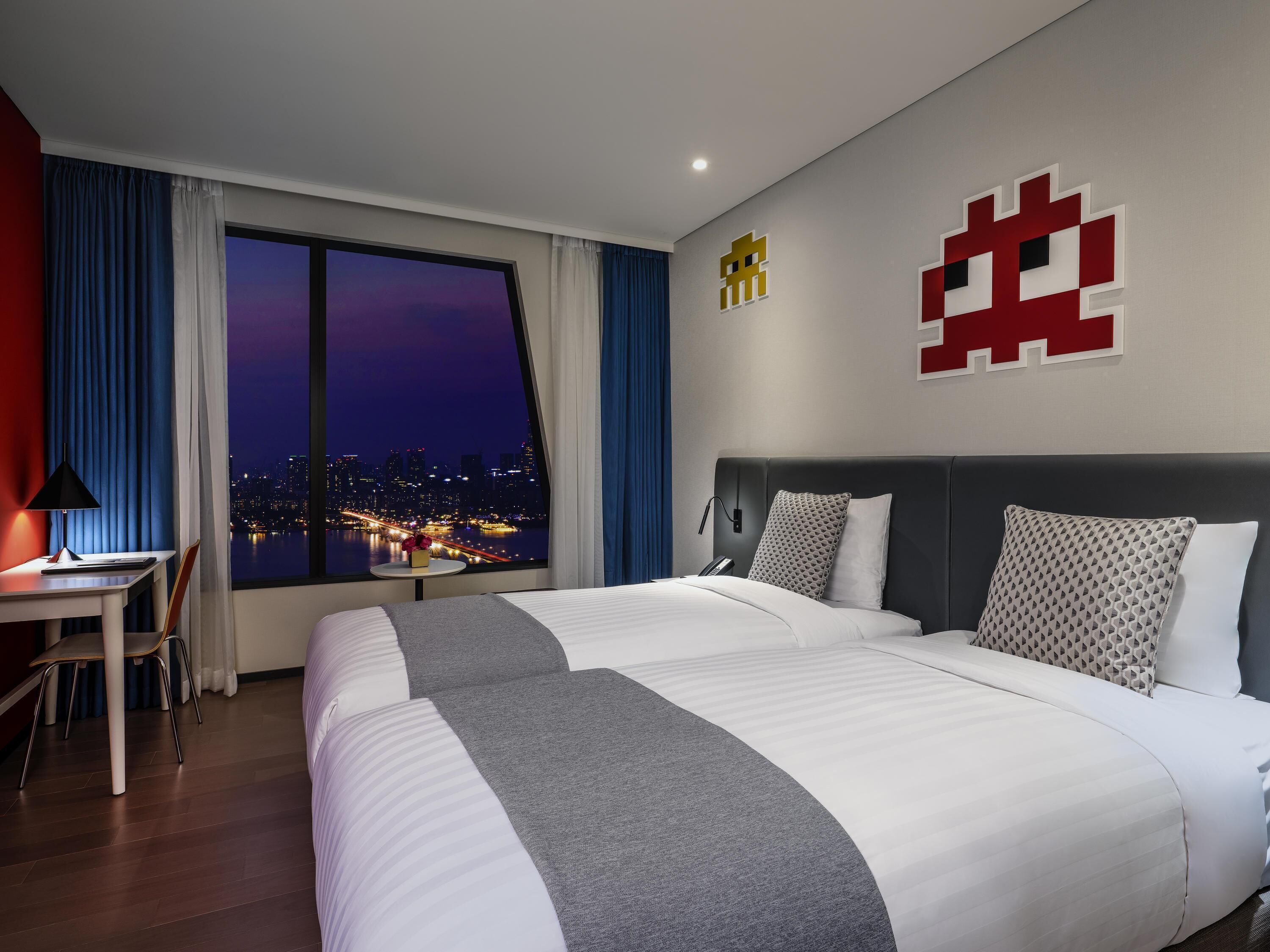 Una habitación de hotel con una cama grande, un escritorio y vistas a un paisaje urbano de noche.