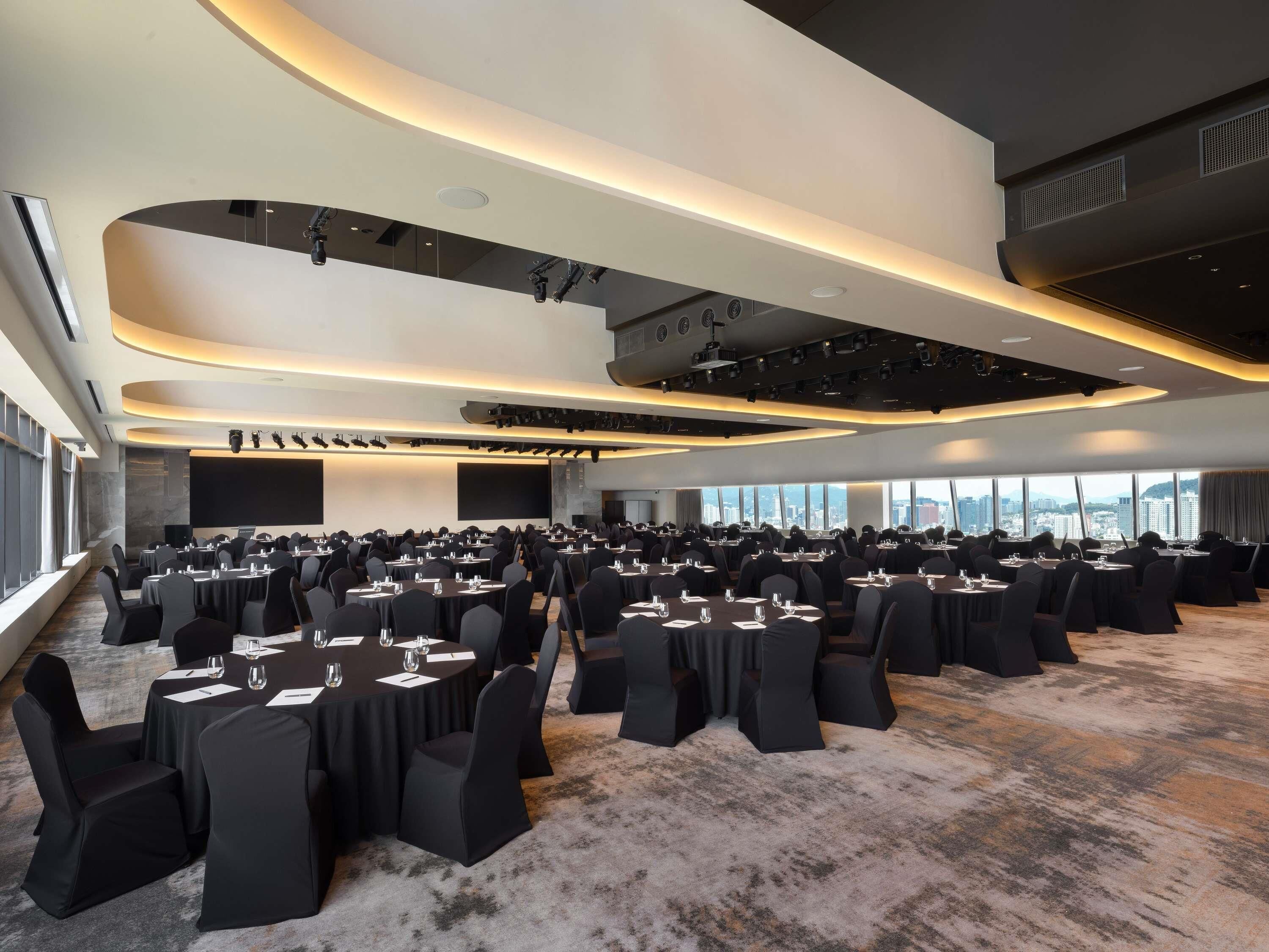 A conference room with multiple tables and chairs, large windows, and a modern ceiling design.
