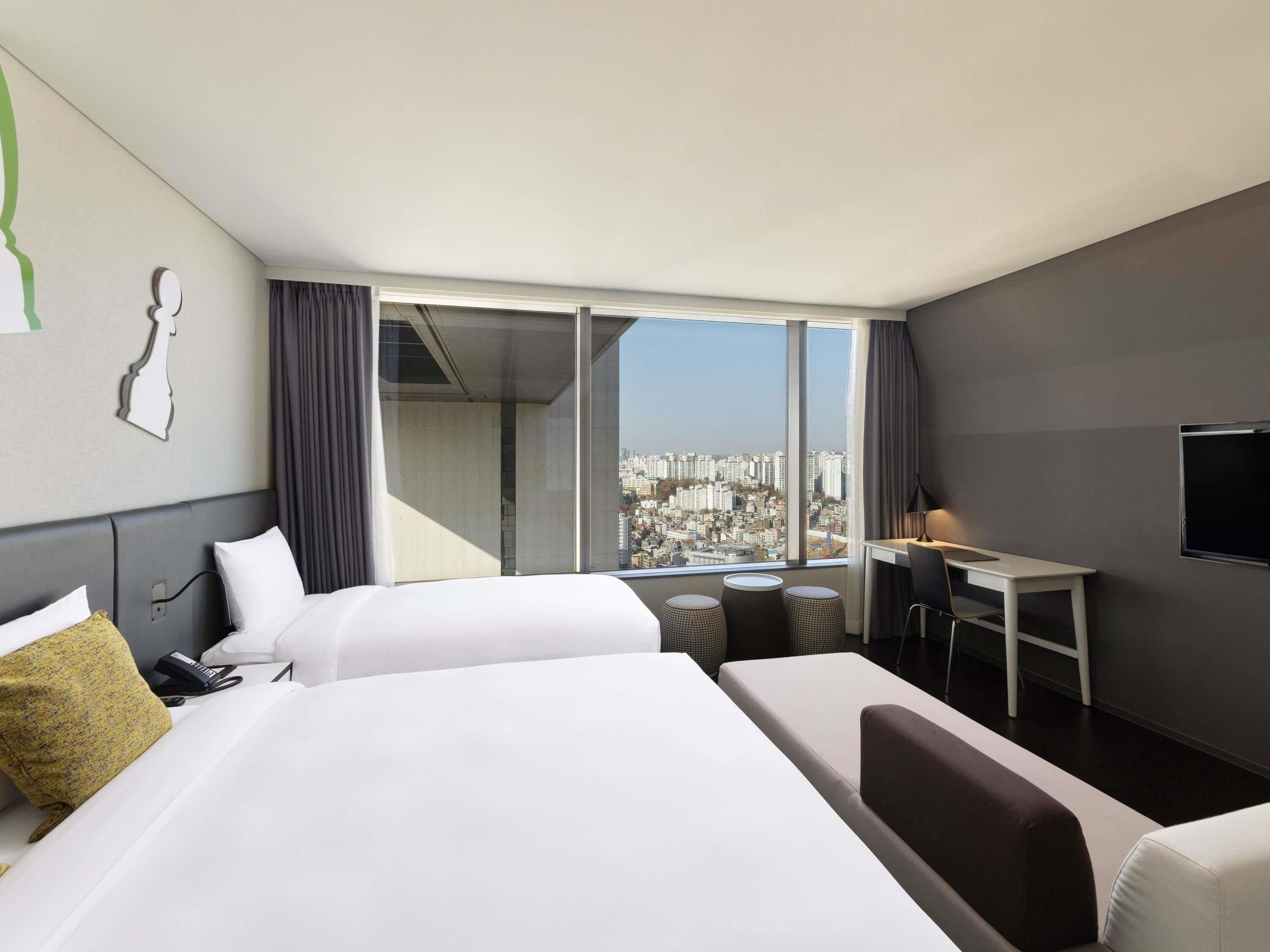 A hotel room with two beds, a desk, a chair, and a TV.