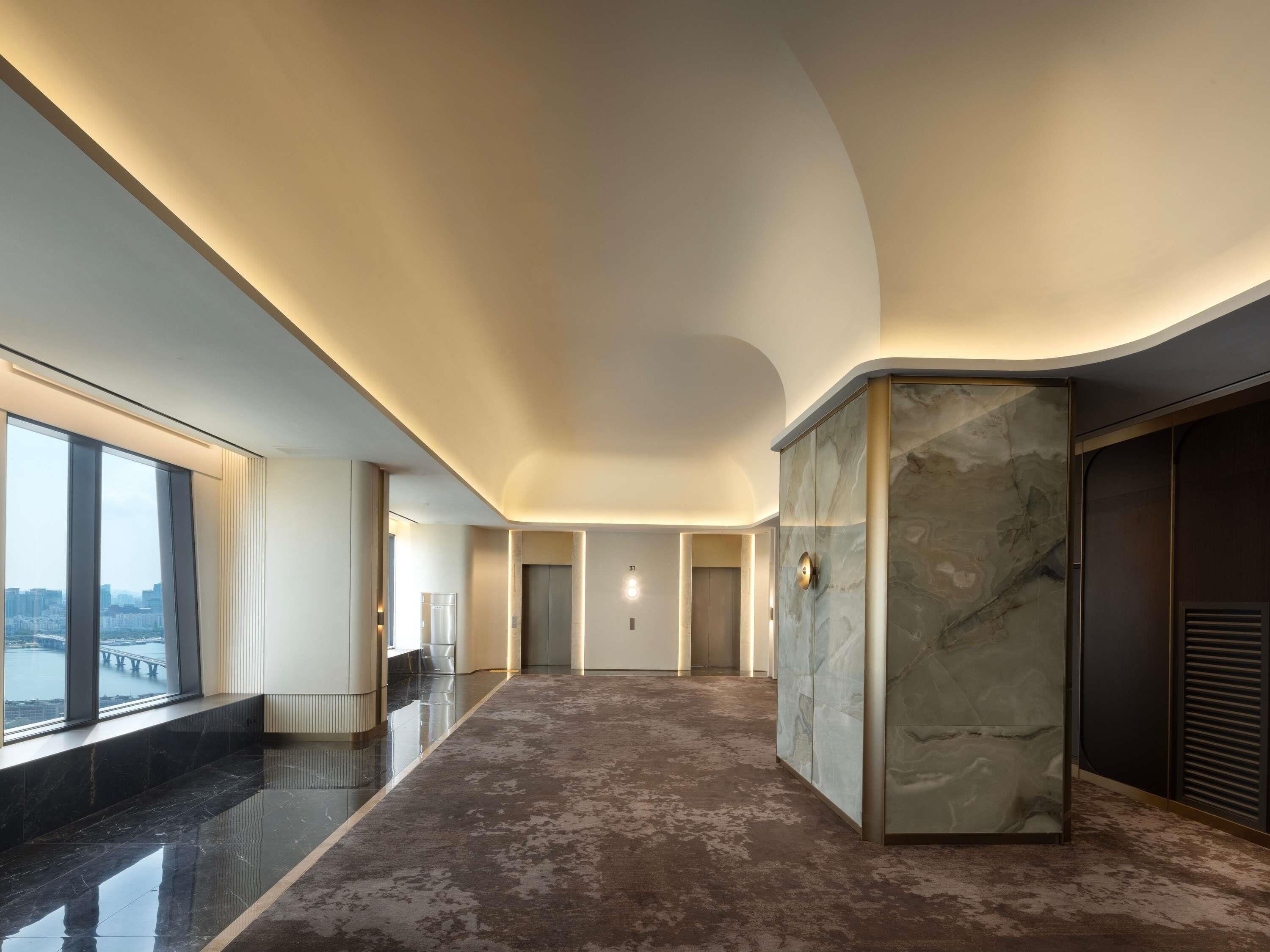 Un hall d’hôtel moderne avec une colonne en marbre, une grande fenêtre donnant sur la ville et un sol ciré.
