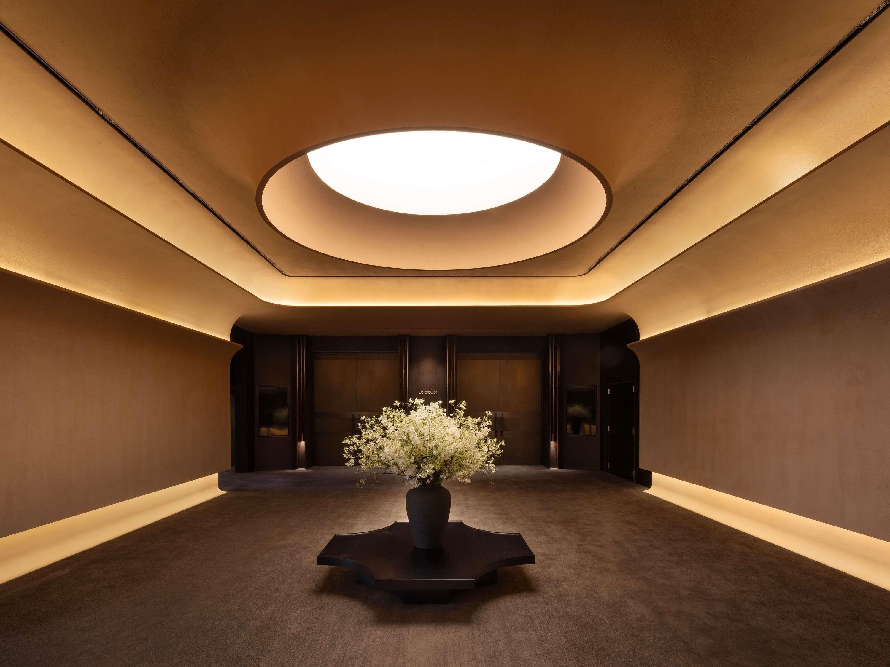 A modern interior with a central floral arrangement on a pedestal, recessed lighting, and a curved ceiling.