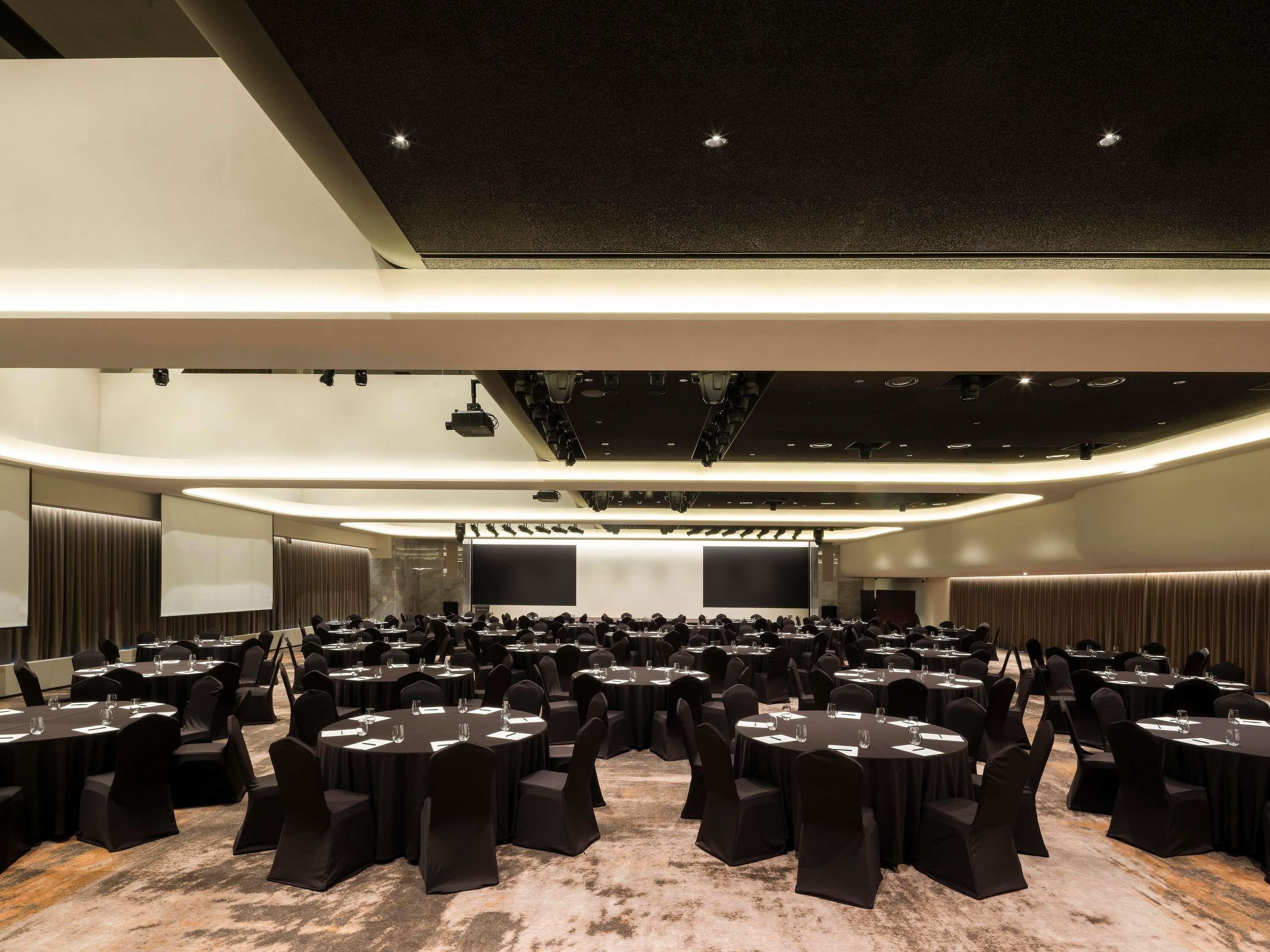 A conference room with round tables, black chairs, and a large screen at the front.