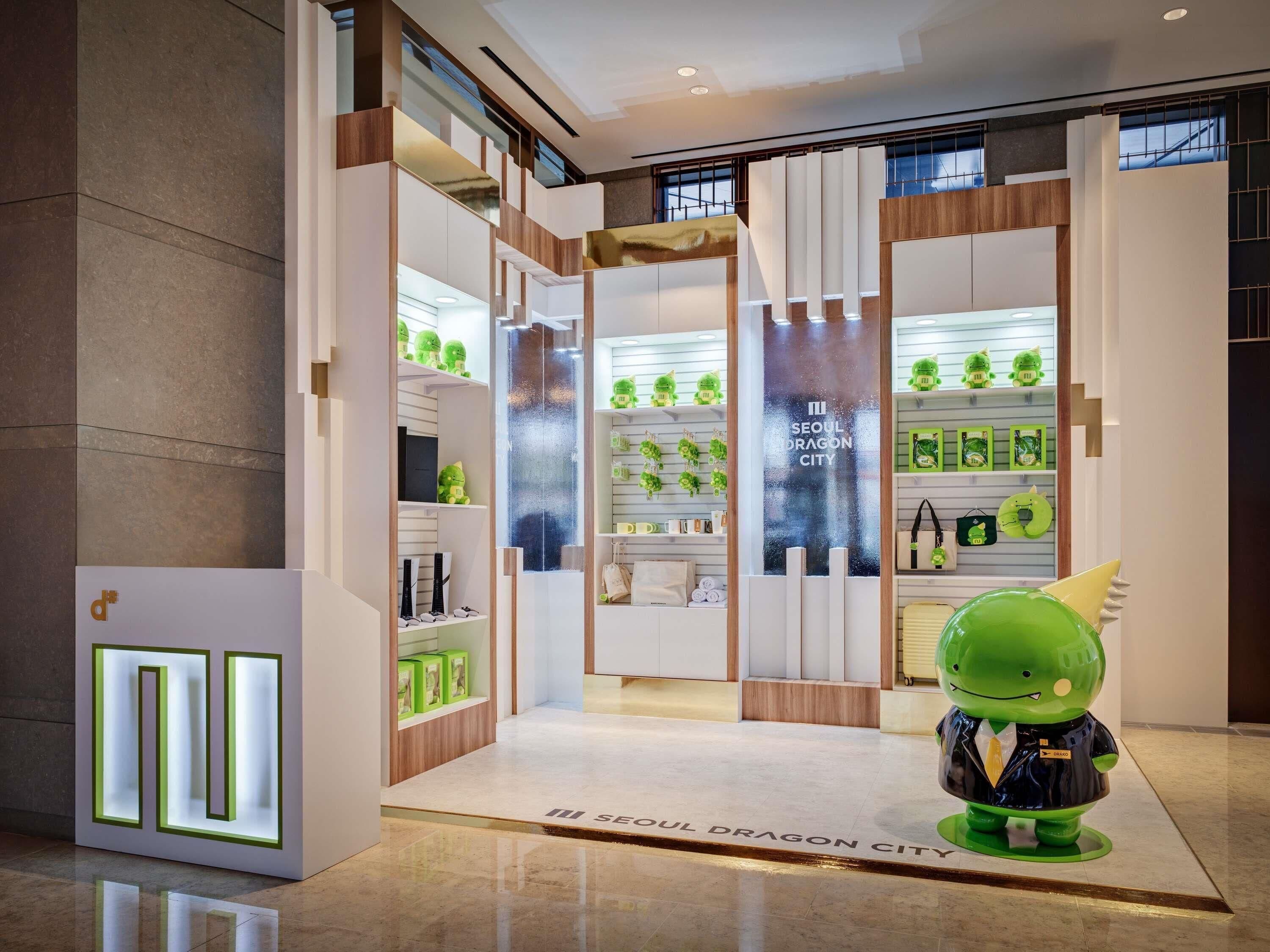 A modern interior with a glass partition, shelves with green plush toys, and a mascot figure.