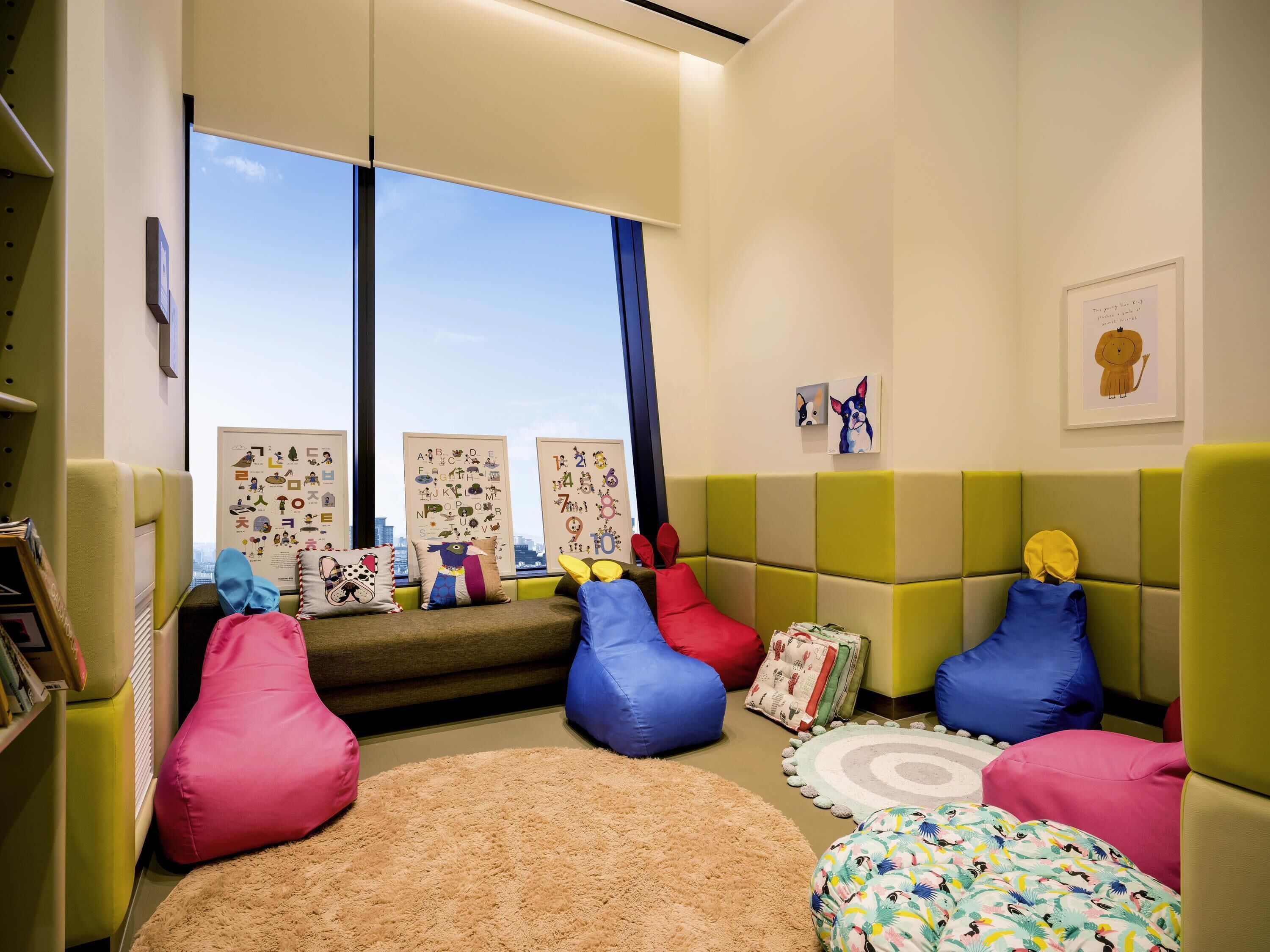 Una habitación acogedora con un sofá, pufs de colores, una alfombra y carteles educativos en la pared.