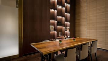 A conference room with a long wooden table, four chairs, and a wall with built-in shelves and lighting.