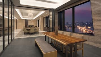 Un comedor moderno con una larga mesa de madera, bancos y vistas a la ciudad a través de grandes ventanales.