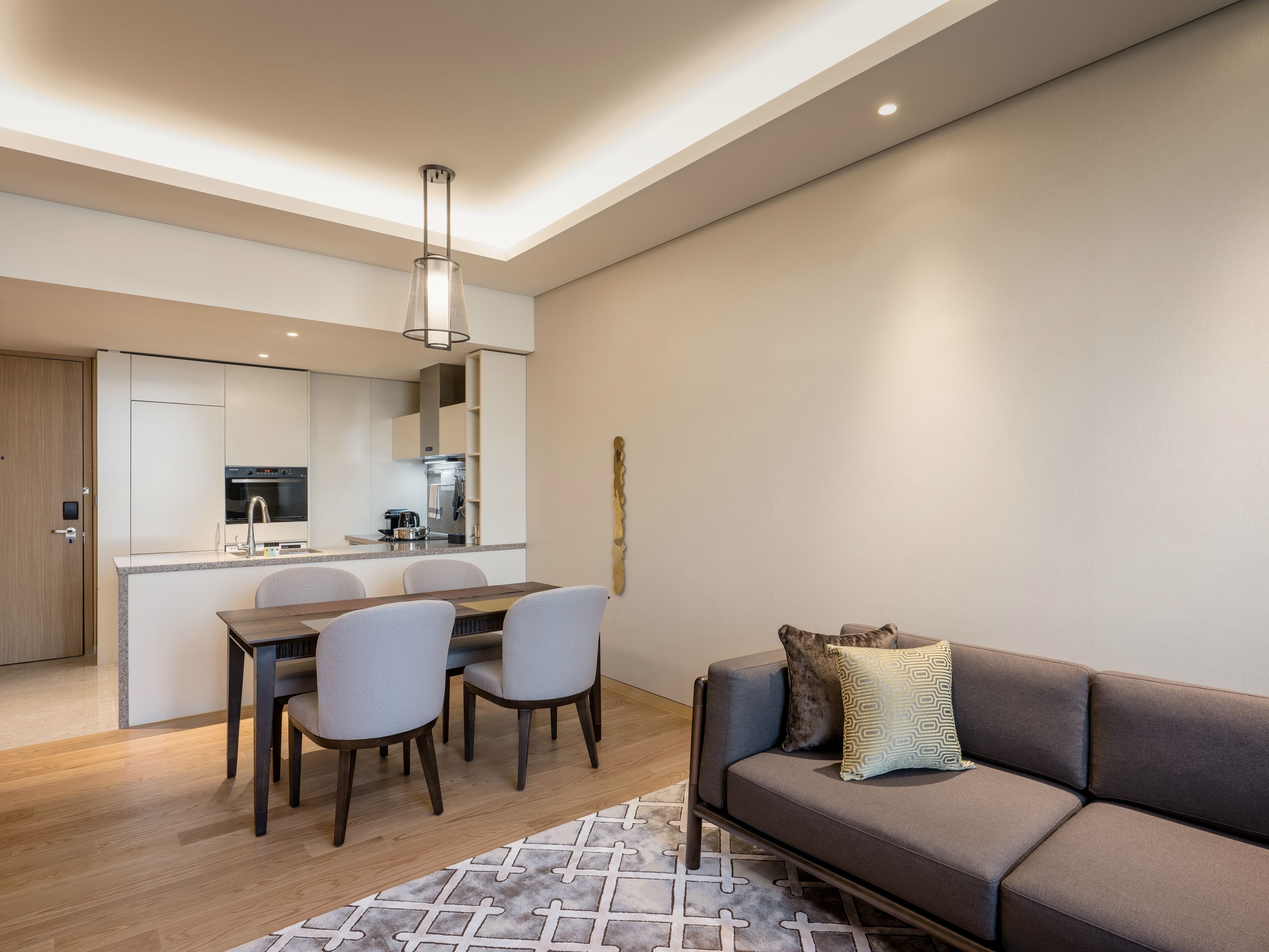 A modern living room with a sofa, a dining table with chairs, a kitchen area with a stove, and a pendant light.