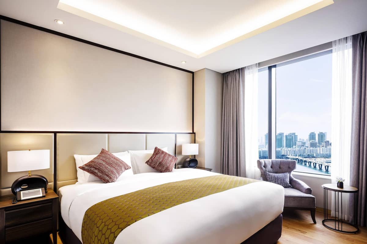Une chambre d’hôtel moderne avec un grand lit, une vue sur la ville, une petite table ronde et une chaise.