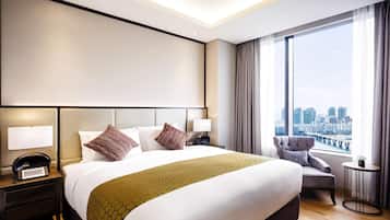 A modern hotel room with a large bed, a city view, a small round table, and a chair.
