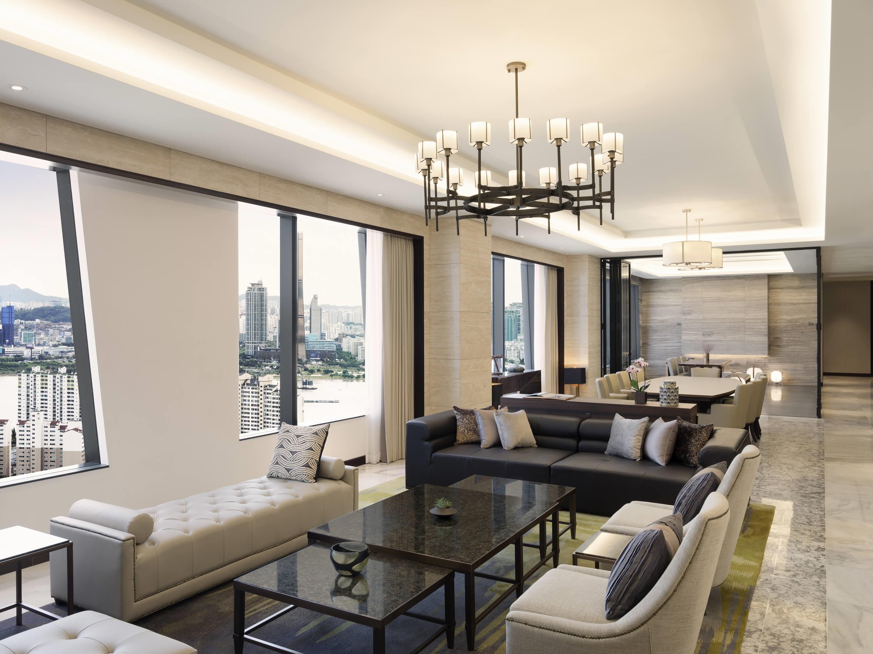 Une chambre d’hôtel moderne offrant une vue imprenable sur la ville, avec un coin repas et un salon comprenant un canapé et une table basse.