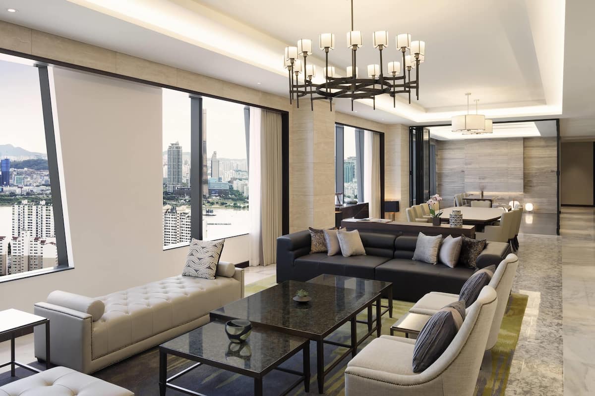 Une chambre d’hôtel moderne offrant une vue imprenable sur la ville, avec un coin repas et un salon comprenant un canapé et une table basse.