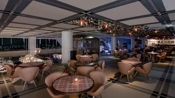 A modern lounge area with round tables and chairs, a checkered ceiling, and a decorative floral arrangement.