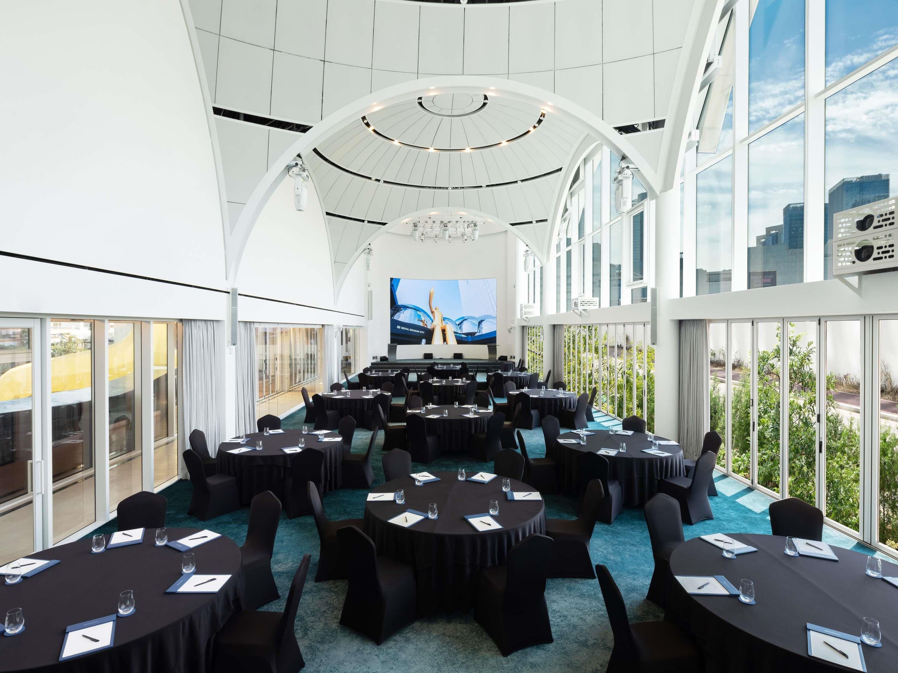 A conference room with multiple tables, a large screen, and large windows offering a city view.