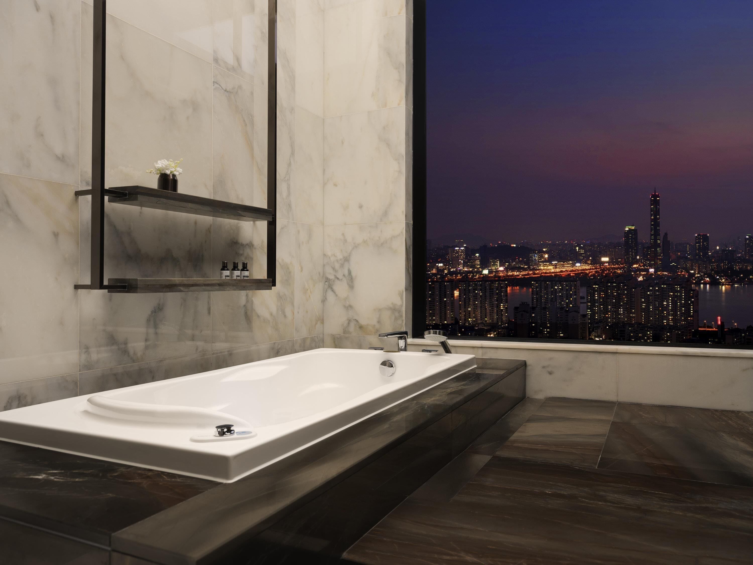 A modern bathroom with a large bathtub, a mirror, and a shelf with toiletries.