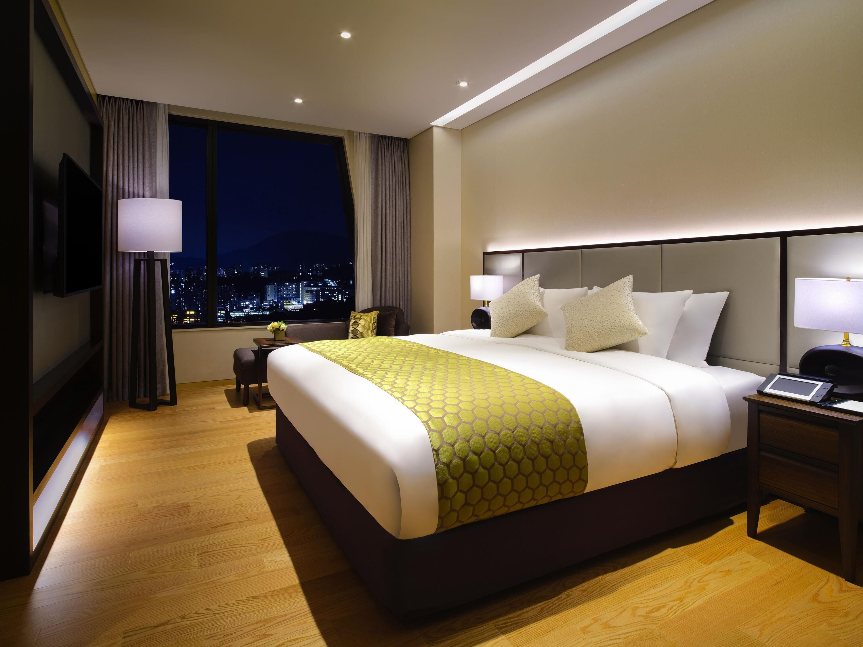 Une chambre d’hôtel avec un grand lit, des tables de chevet, une télévision et une vue sur la ville.
