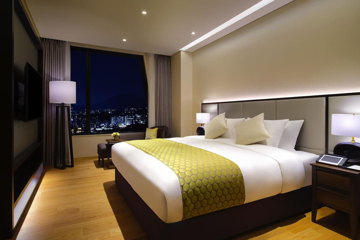 Une chambre d’hôtel avec un grand lit, un bureau, une chaise, une télévision et une fenêtre donnant sur la ville.