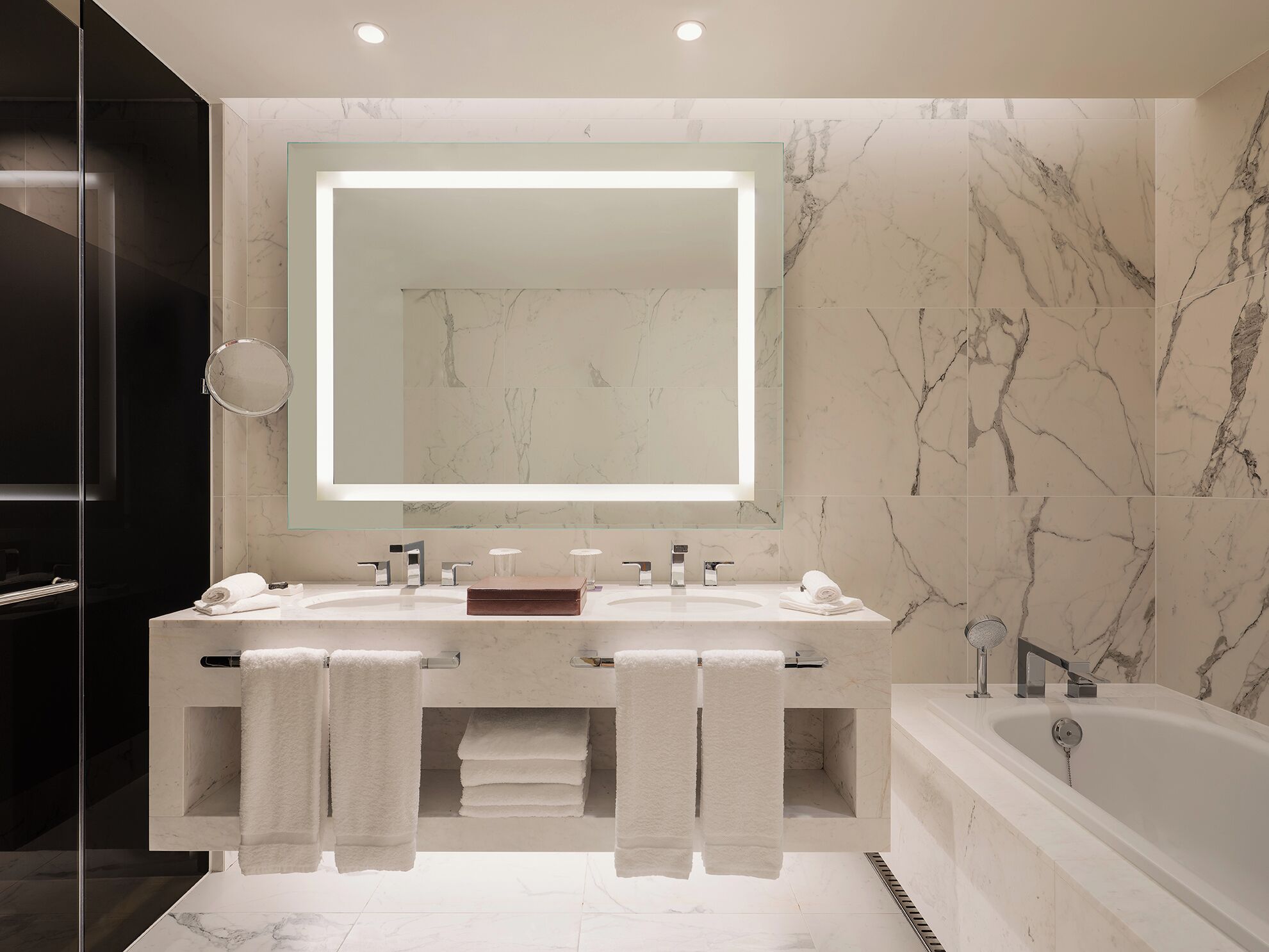 A modern bathroom with two sinks, a large mirror, and a bathtub.