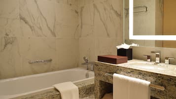 A bathroom with a bathtub, marble walls, a granite countertop, a sink, a mirror, and a towel rack.