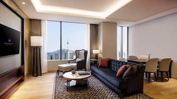 Habitación de hotel moderna con sofá, mesa de comedor, sillas, televisor y ventanas amplias con vista a la ciudad.