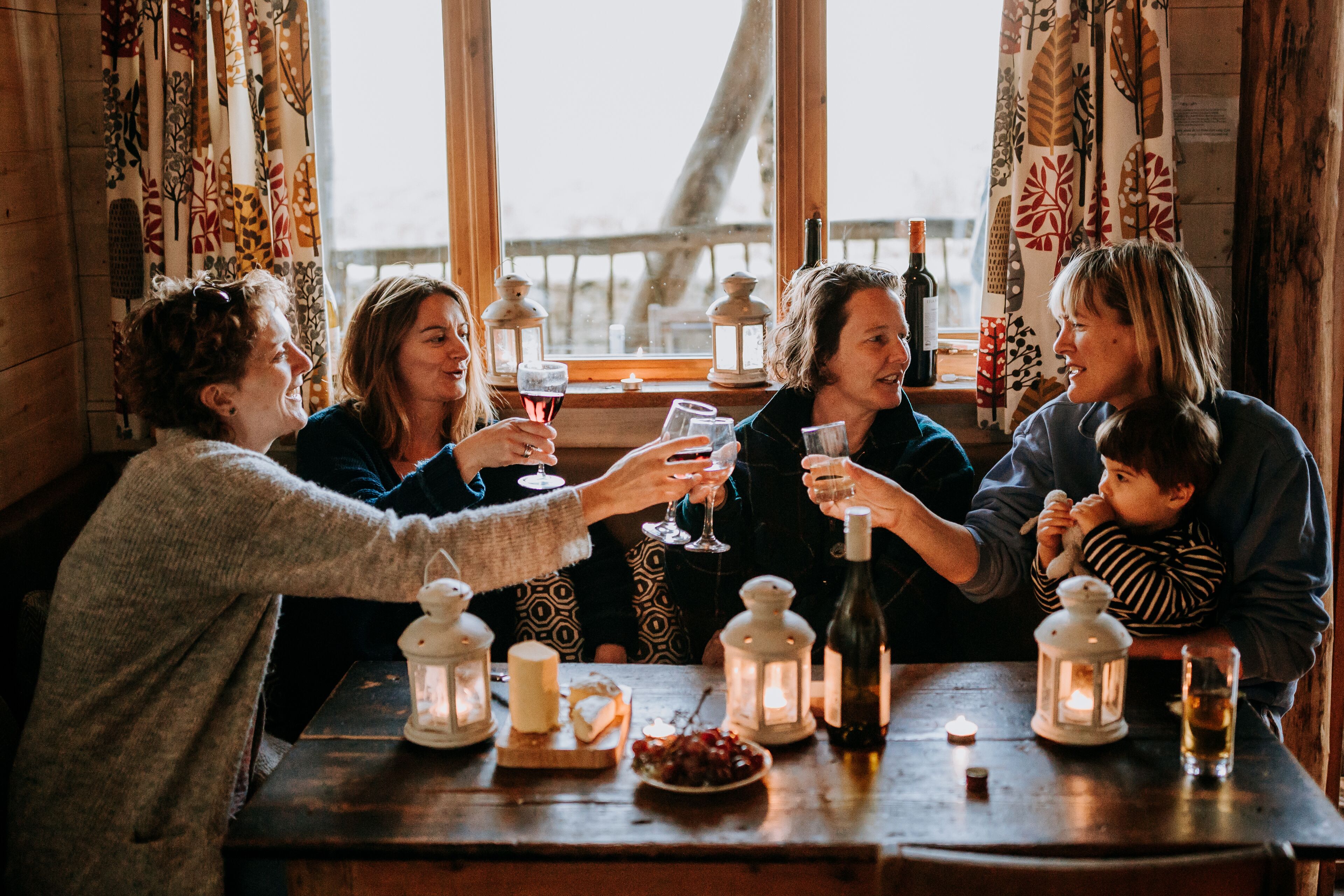 A group of people seated around a wooden table with candles and bottles, suggesting a social gathering or celebration.