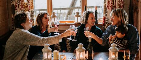 A group of people seated around a wooden table with candles and bottles, suggesting a social gathering or celebration.