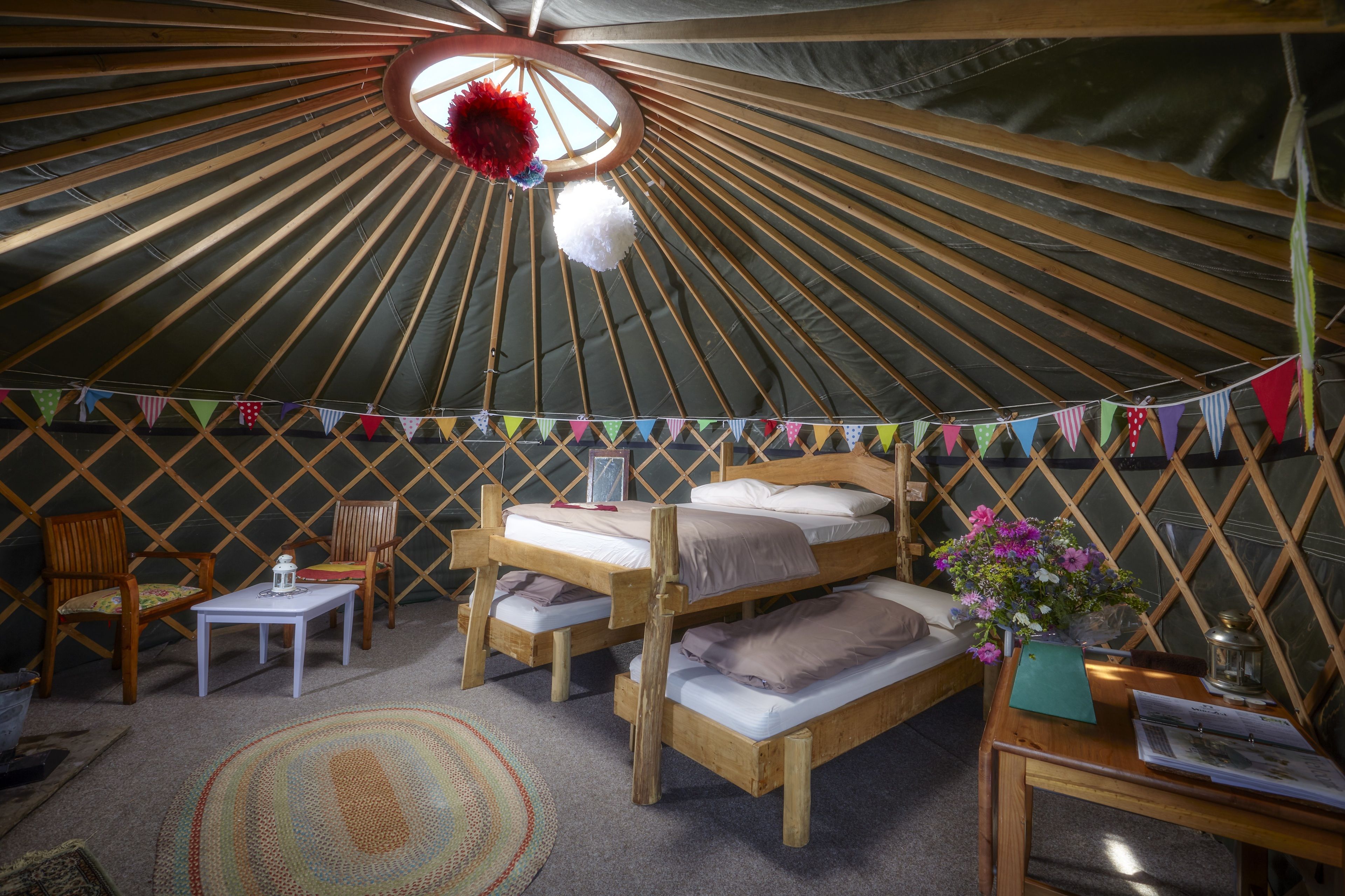 Interieur van een joert met een rond plafond, houten bedden, een kleine tafel en een stoel.