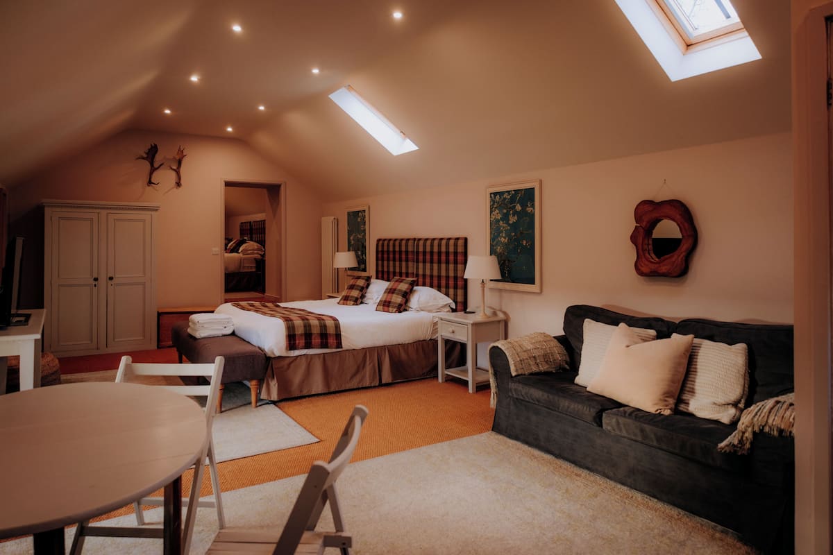 A bedroom with a bed, a sofa, a table, and a skylight.