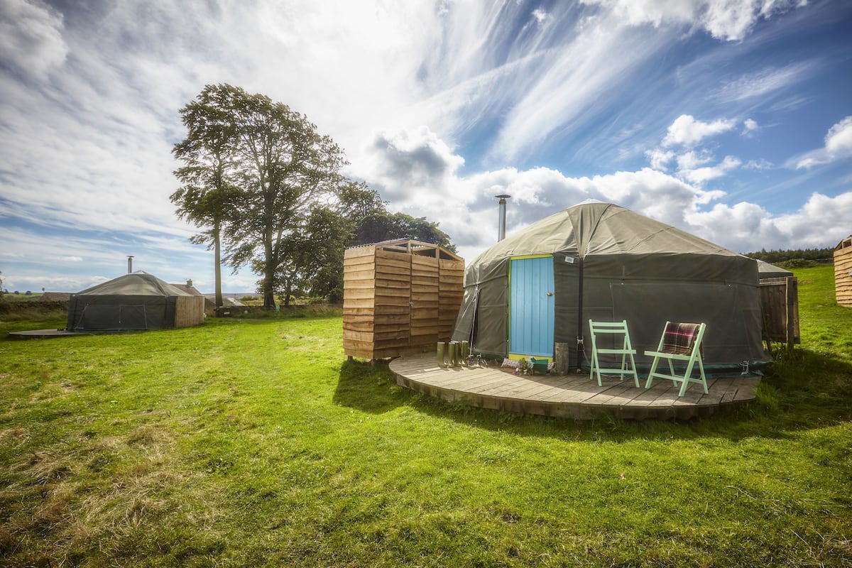 A yurt with a blue door, a wooden structure, and a small porch with two chairs.