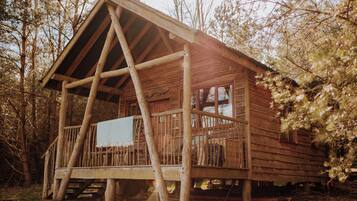 A rustic wooden cabin with a porch, surrounded by trees.