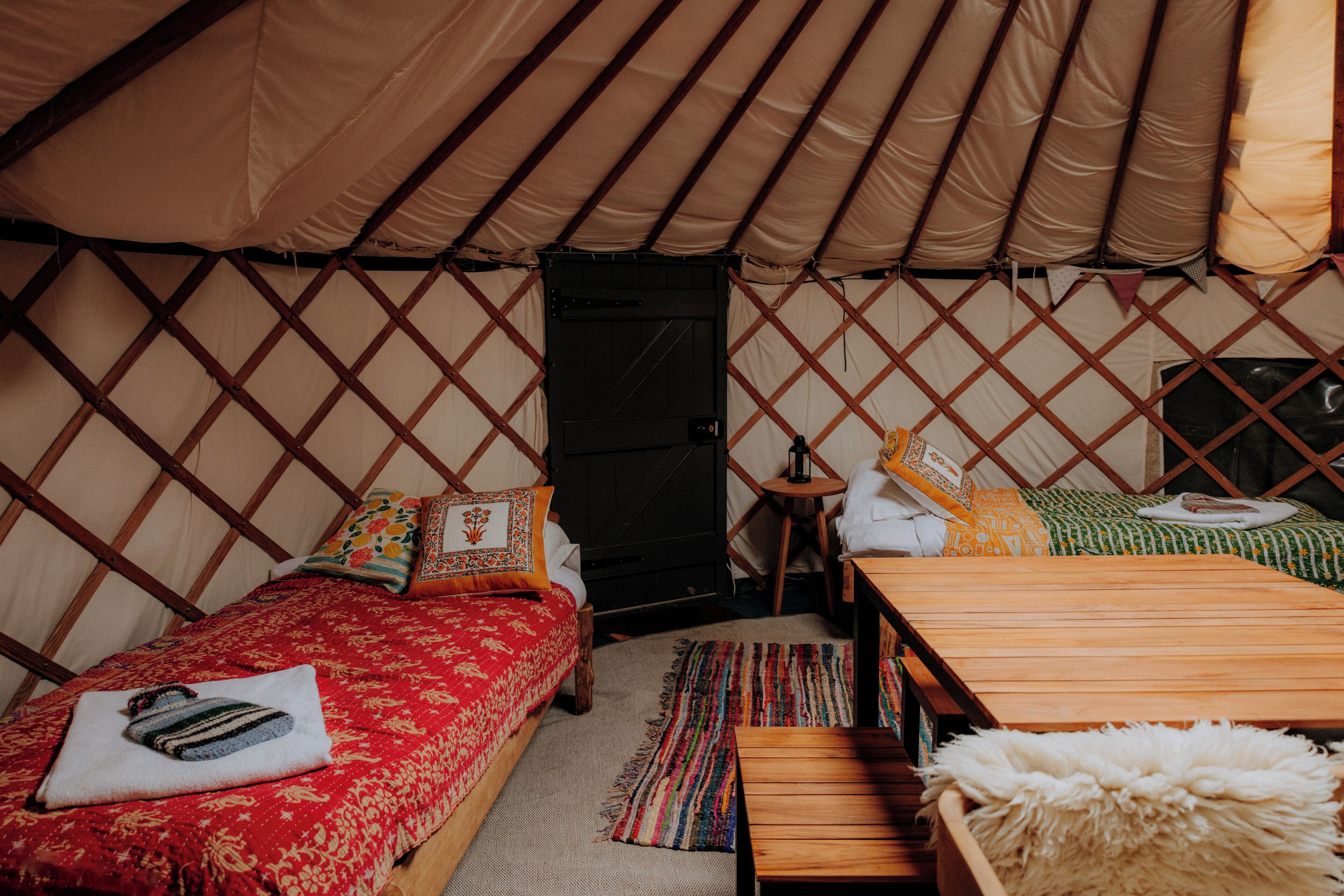A cozy interior of a yurt with a bed, a small table, and a bench.