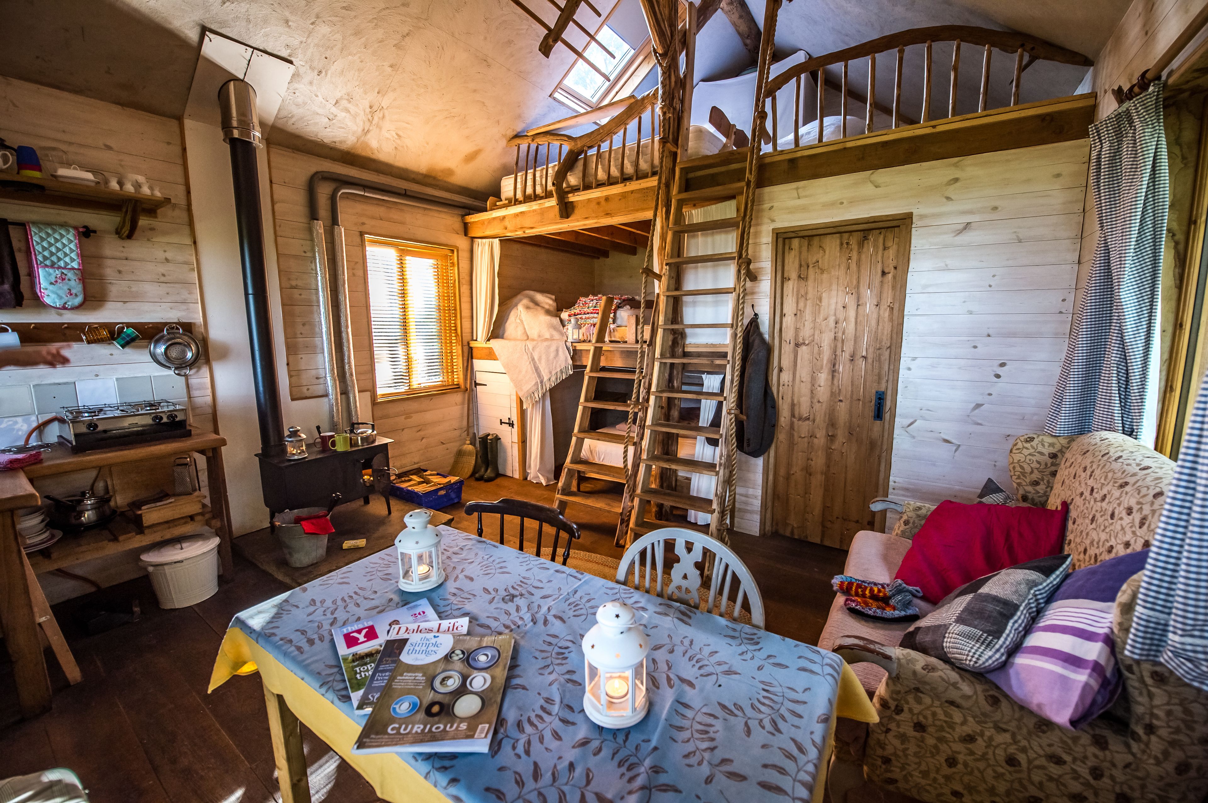 A rustic cabin interior with a loft bedroom, wooden furniture, a dining table with a menu, and a cozy seating area.