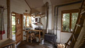 A rustic kitchen with wooden floors, a stove, and a window overlooking greenery. - Swinton Bivouac (Ripon)