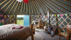 A yurt interior with a bed, wooden furniture, a stove, and colorful decorations. - Swinton Bivouac (Ripon)
