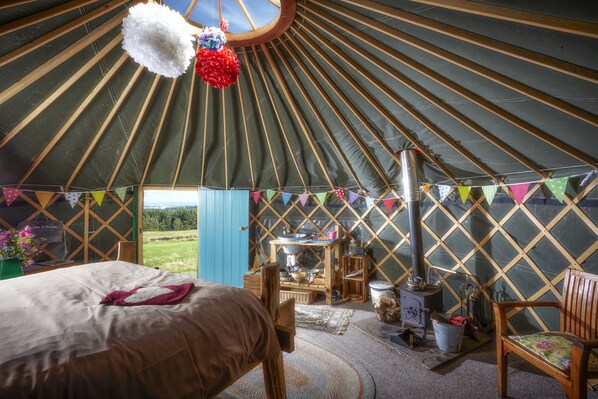 A yurt interior with a bed, wooden furniture, a stove, and colorful decorations.
