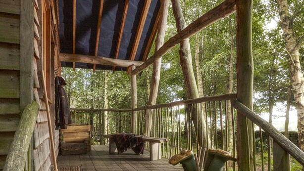 A wooden deck with a bench and a covered area, surrounded by trees. - Swinton Bivouac (Ripon)