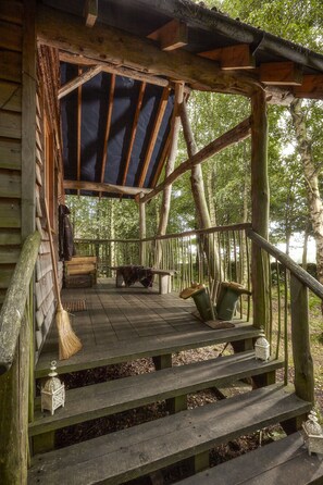 A wooden deck with a bench and a covered area, surrounded by trees.
