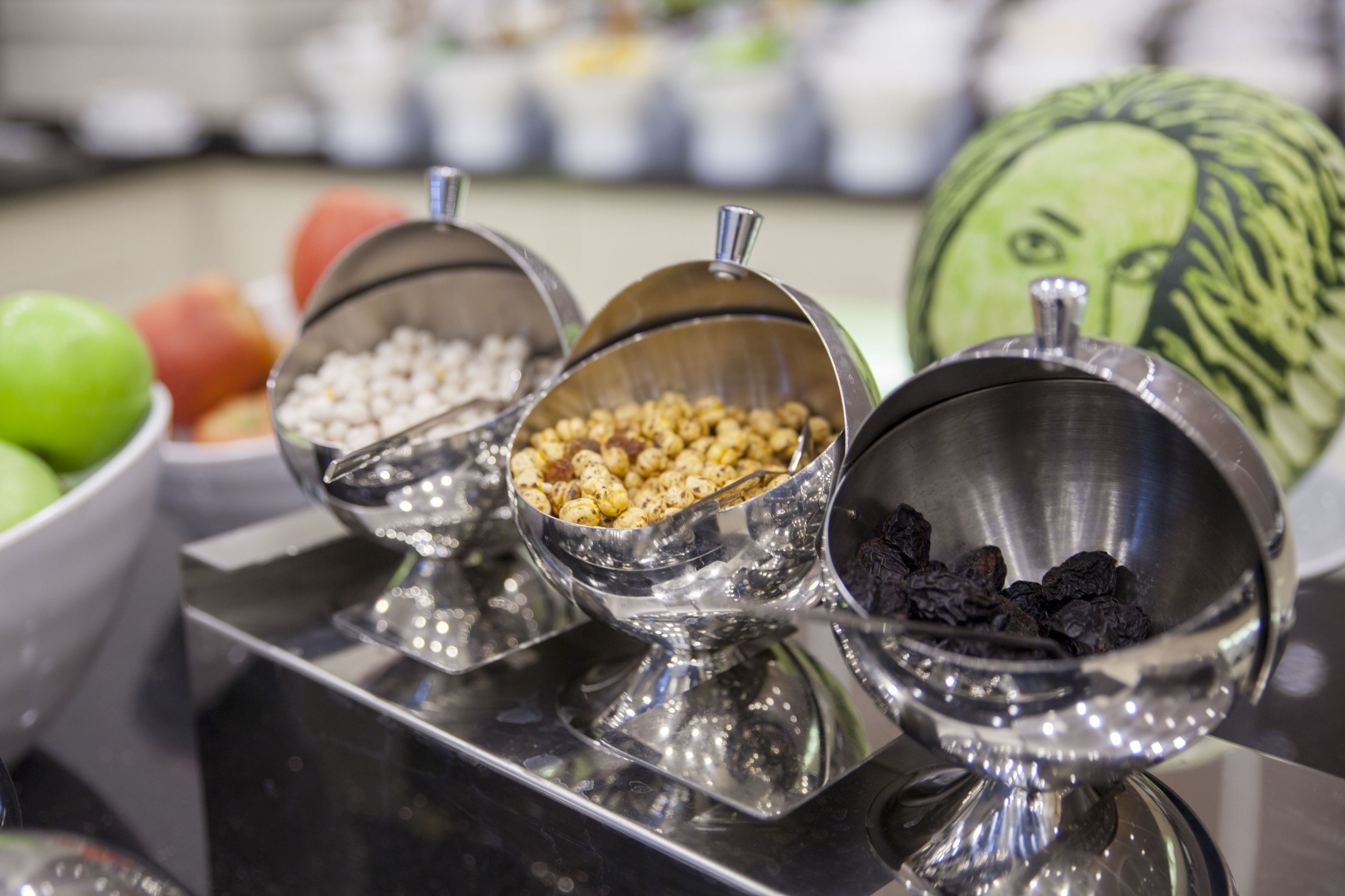 Un bufé con diversos alimentos en recipientes metálicos, entre ellos frutas y frutos secos.