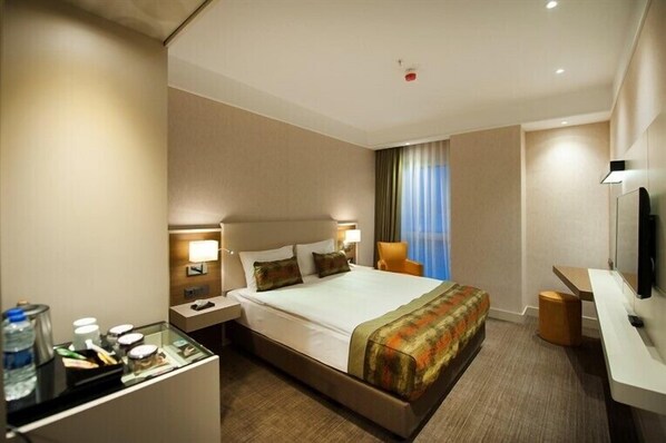 A hotel room with a large bed, bedside tables, a desk, a chair, a television, and a window with curtains.
