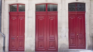Tres puertas rojas con diseños intrincados, en un edificio de piedra.